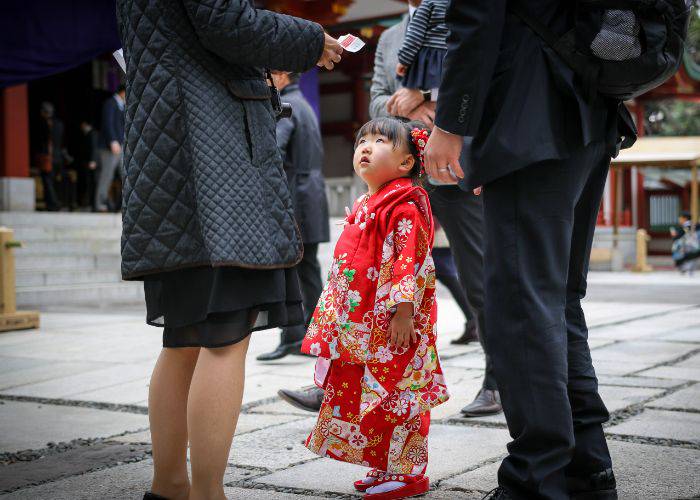 A little girl wearing a colorful kimono looking up at adults.